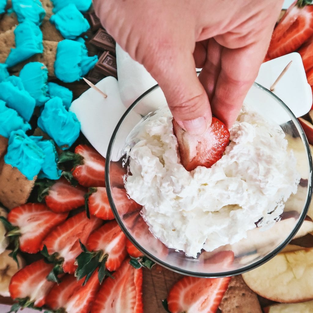 dipping a strawberry into fluffy cream cheese fruit dip