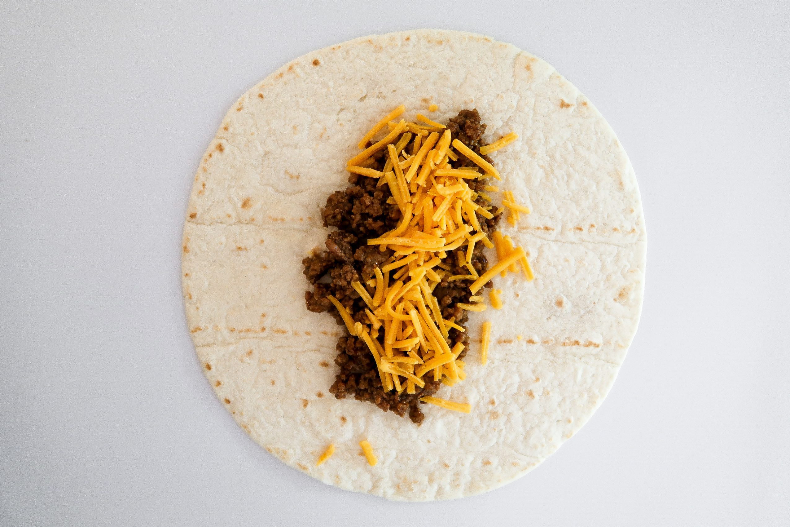 adding the taco meat and shredded cheese to soft shell
