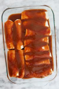 pouring remainder of enchilada sauce on top of enchiladas