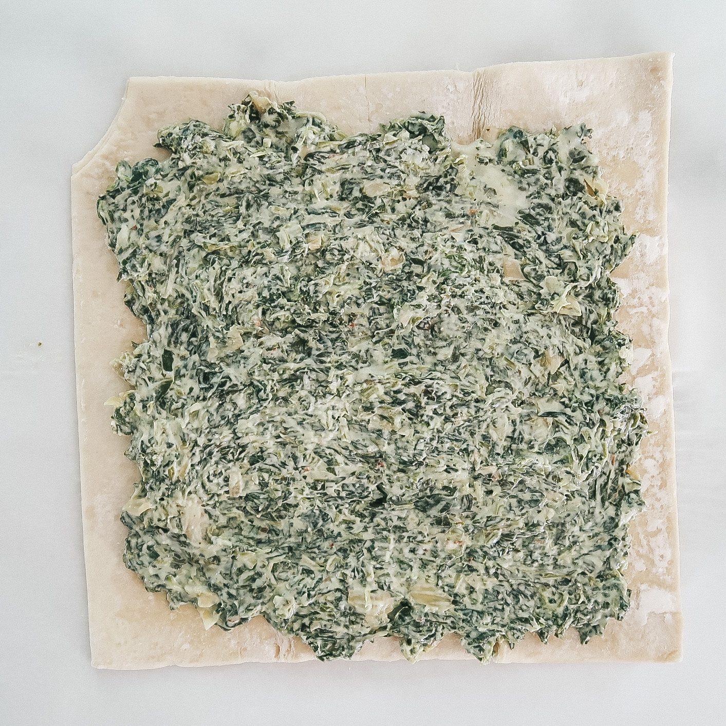 spreading the creamy spinach and artichoke dip onto the dough sheet