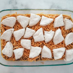 adding the quartered biscuits on top of the shredded cheese