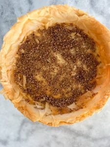 adding the crushed pecans and cinnamon and sugar topping to the cheesecake
